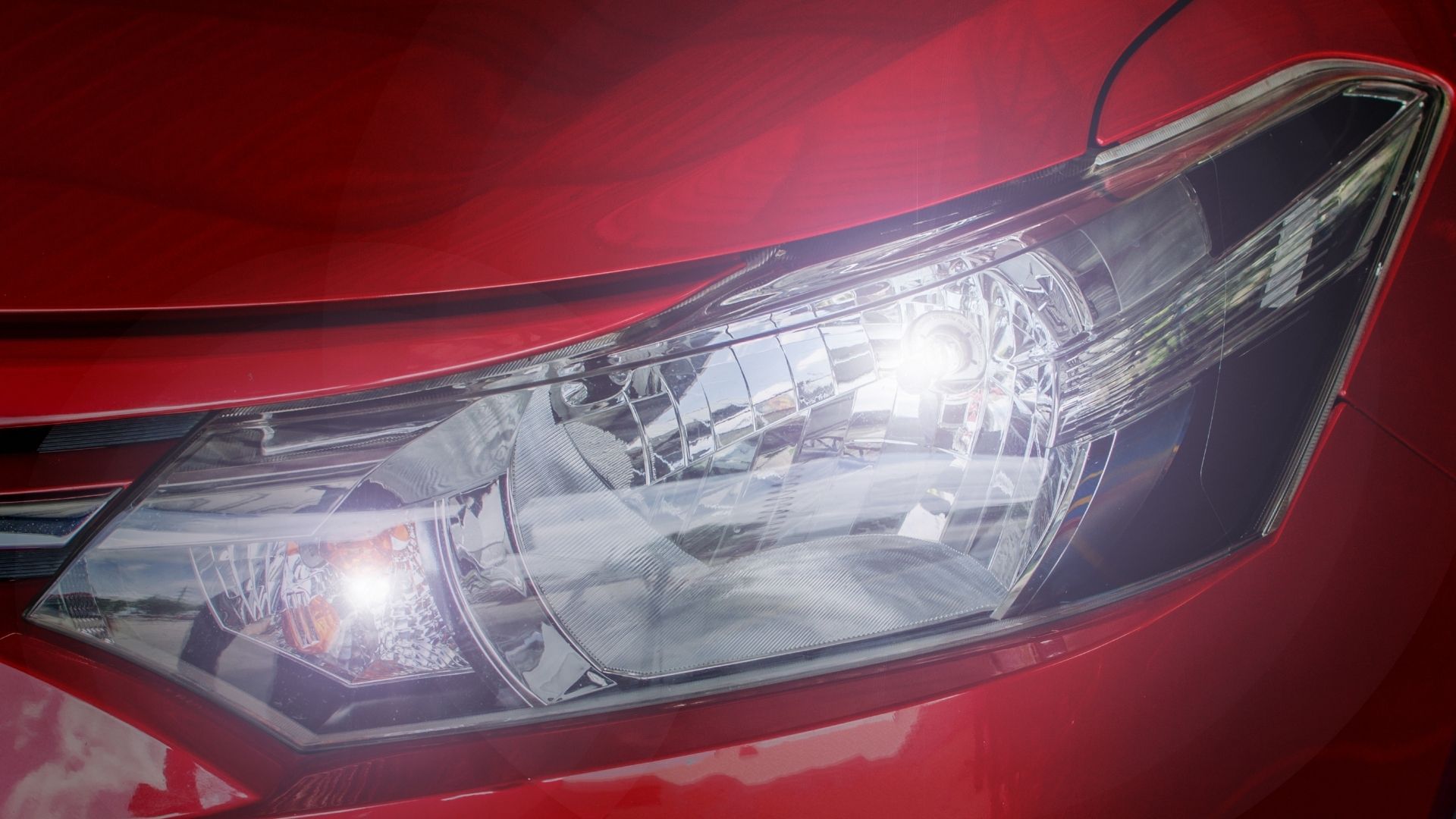 Close-up of a red car’s front headlight with chrome and reflective lens detail