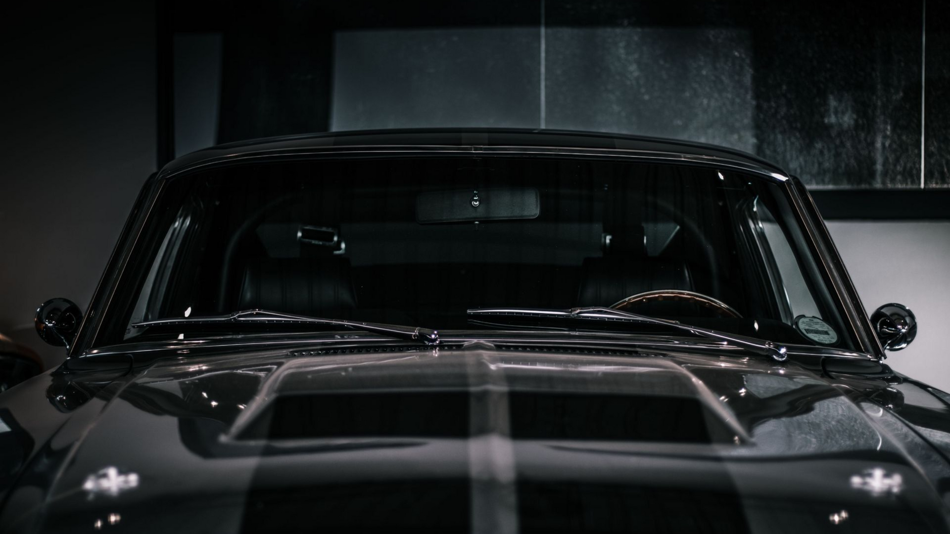 Front view of a black classic car in a dark garage with headlights off
