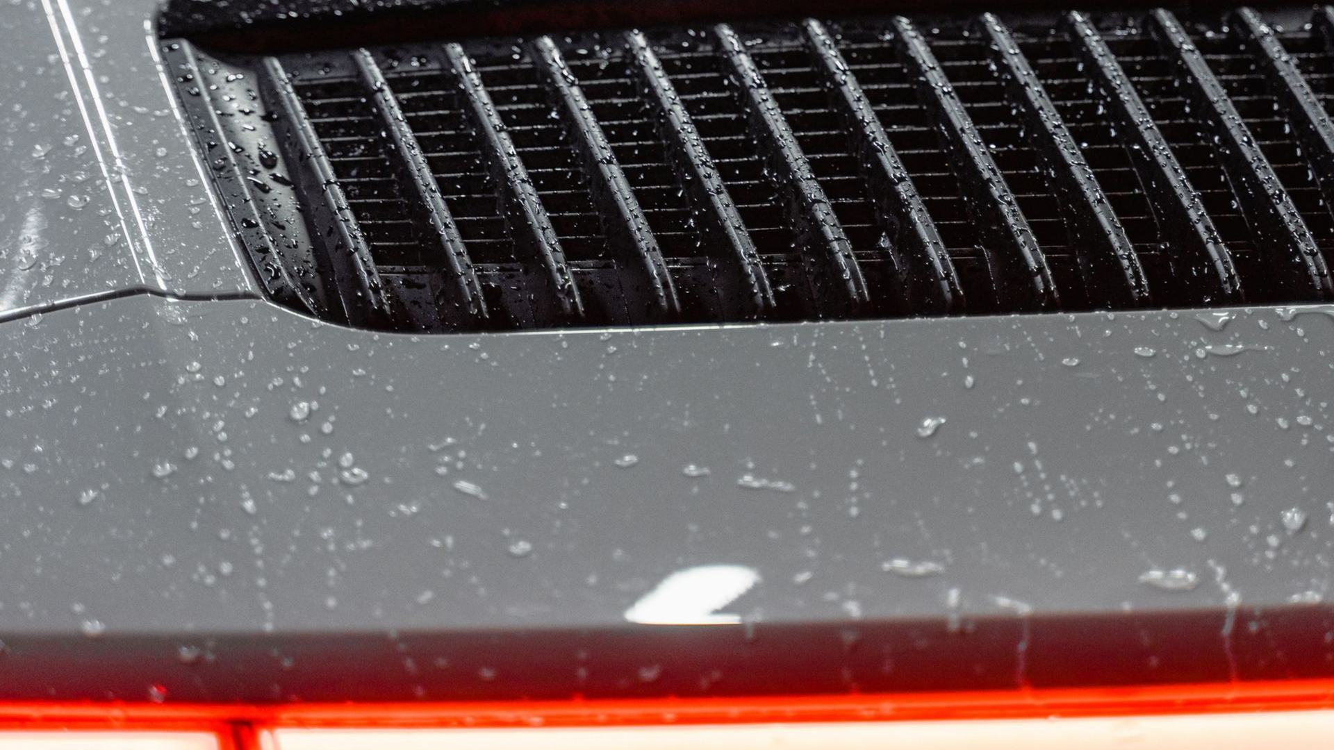 Close-up of a dusty gray car hood with black grille vents and a red light reflection below