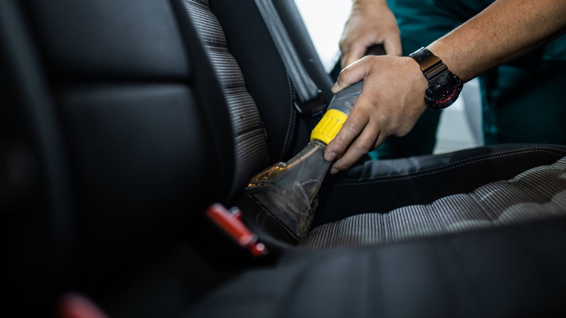 Person cleaning a car seat with a vacuum cleaner inside the vehicle