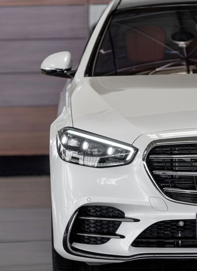 Front view of a white Mercedes-Benz sedan in a showroom, showing the left headlight and grille