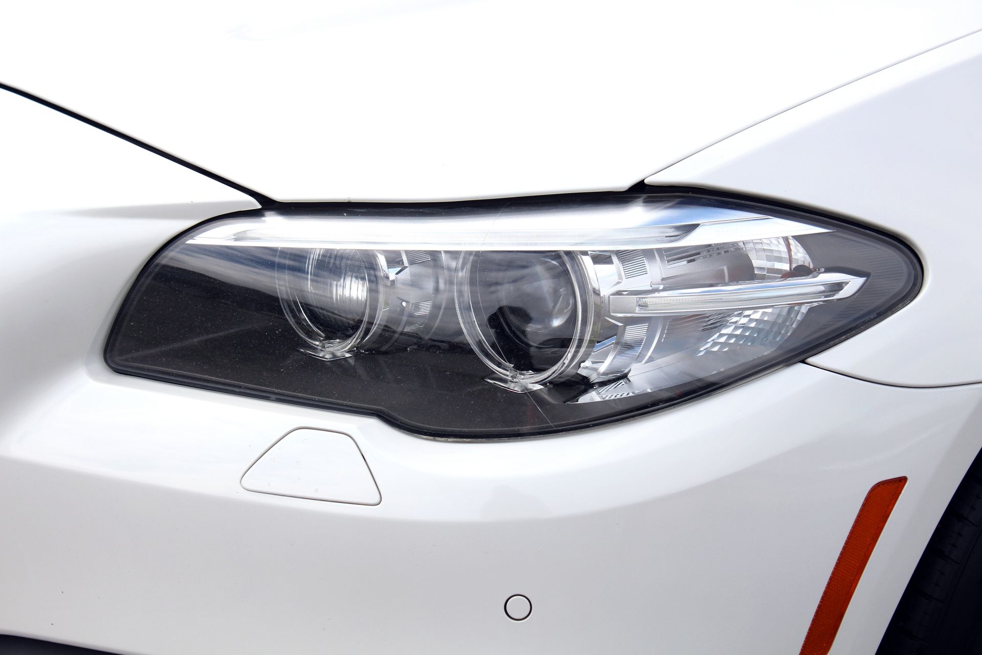 Close-up of a black car’s front headlight and hood with glossy reflections