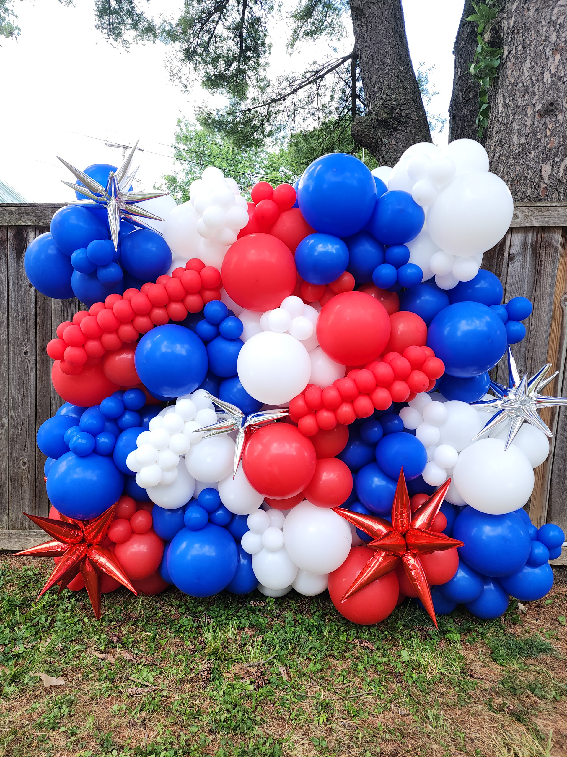 A wall of red , white , and blue balloons sitting on top of a lush green field.