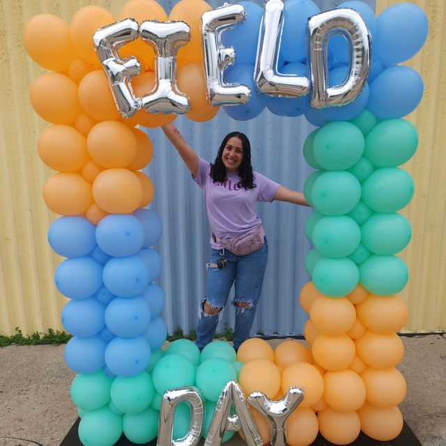 A woman is standing under a balloon arch that says field day