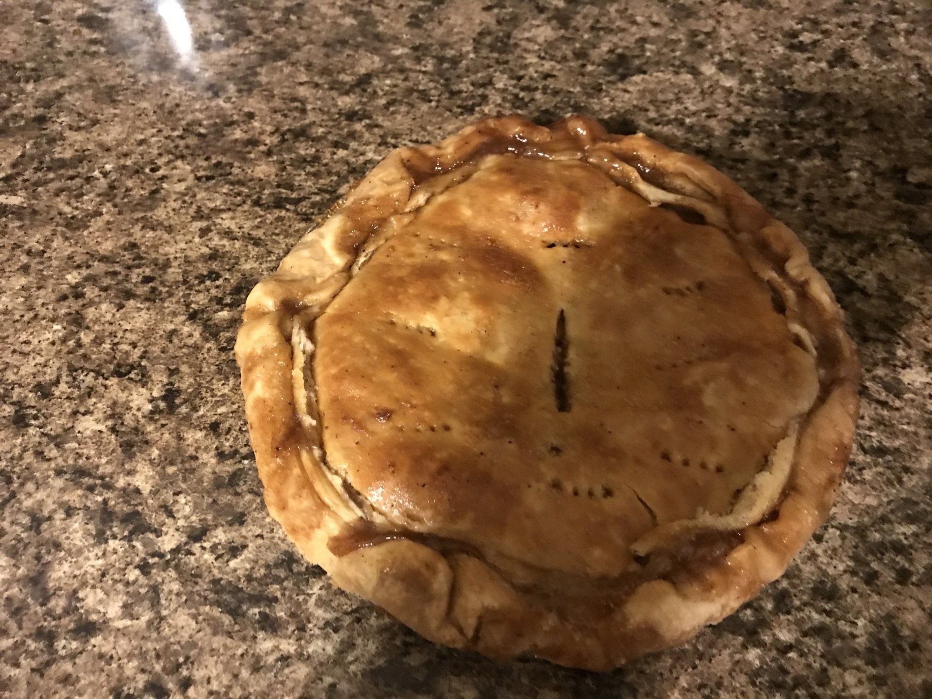Golden-brown baked pie on a speckled countertop, with a slit in the center