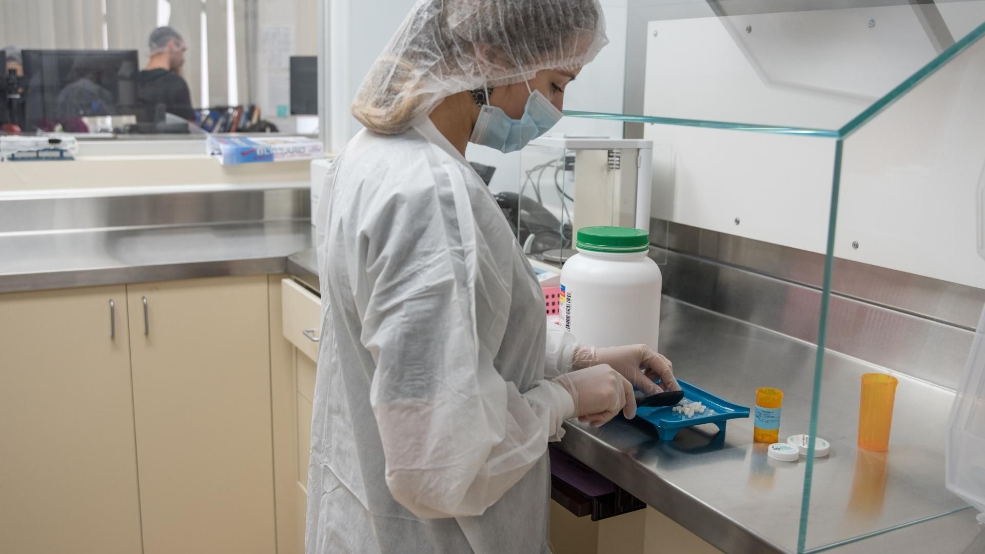 Sterile compounding pharmacy technician in PPE under a containment hood