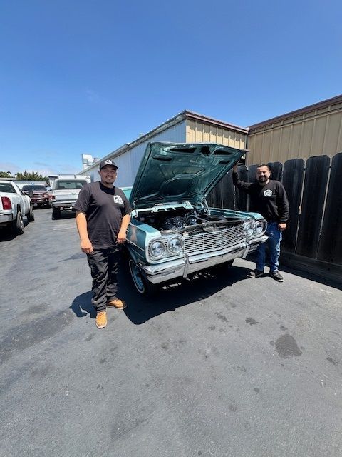 Two men standing next to a car with the hood up