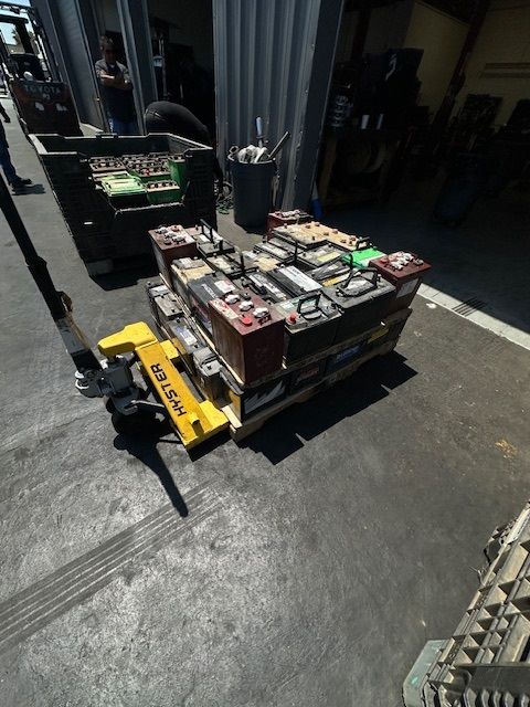 A yellow hand truck carrying a pallet of batteries