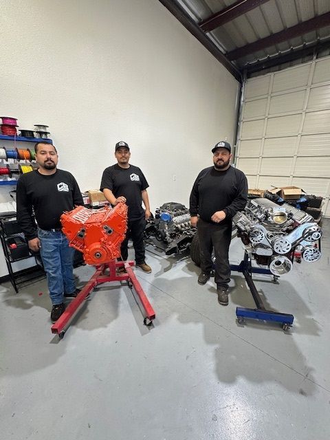 Three men are standing next to a red engine in a garage.
