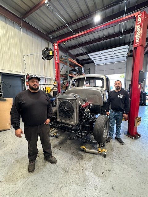 Two men are standing next to a truck in a garage.