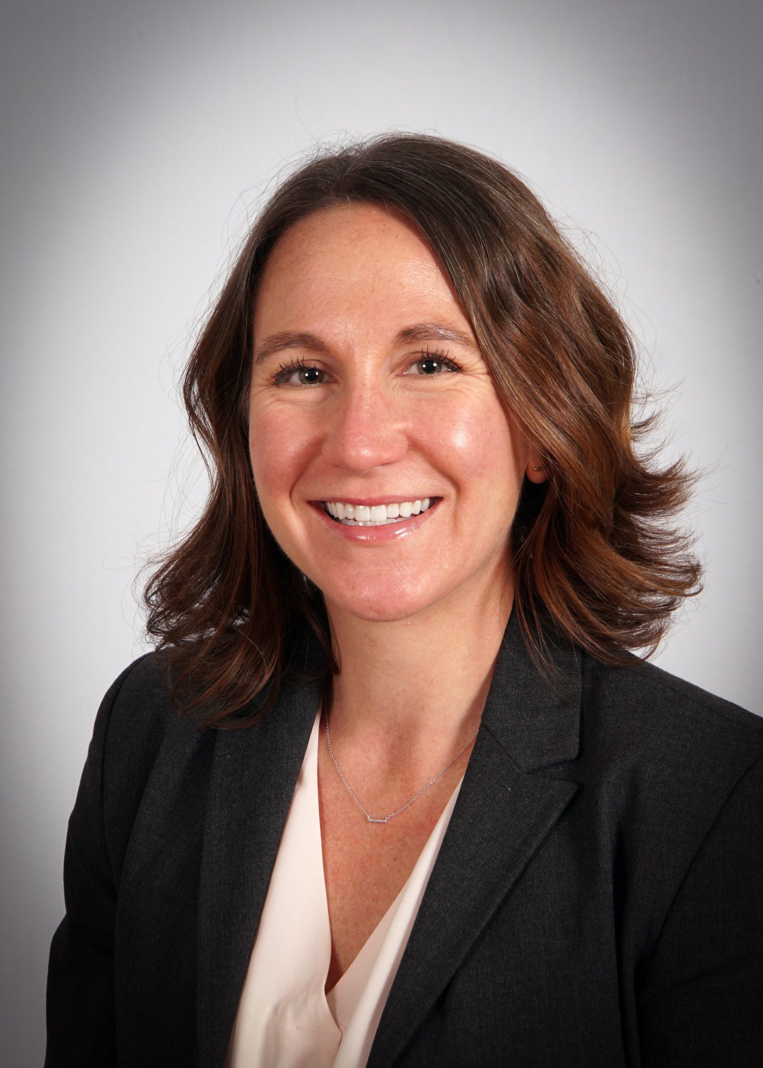 Woman with brown hair and a blazer smiles, headshot.