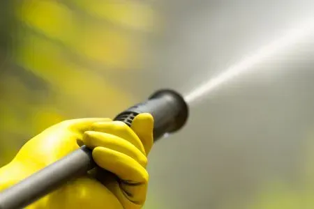 A person wearing yellow gloves is holding a high pressure washer.