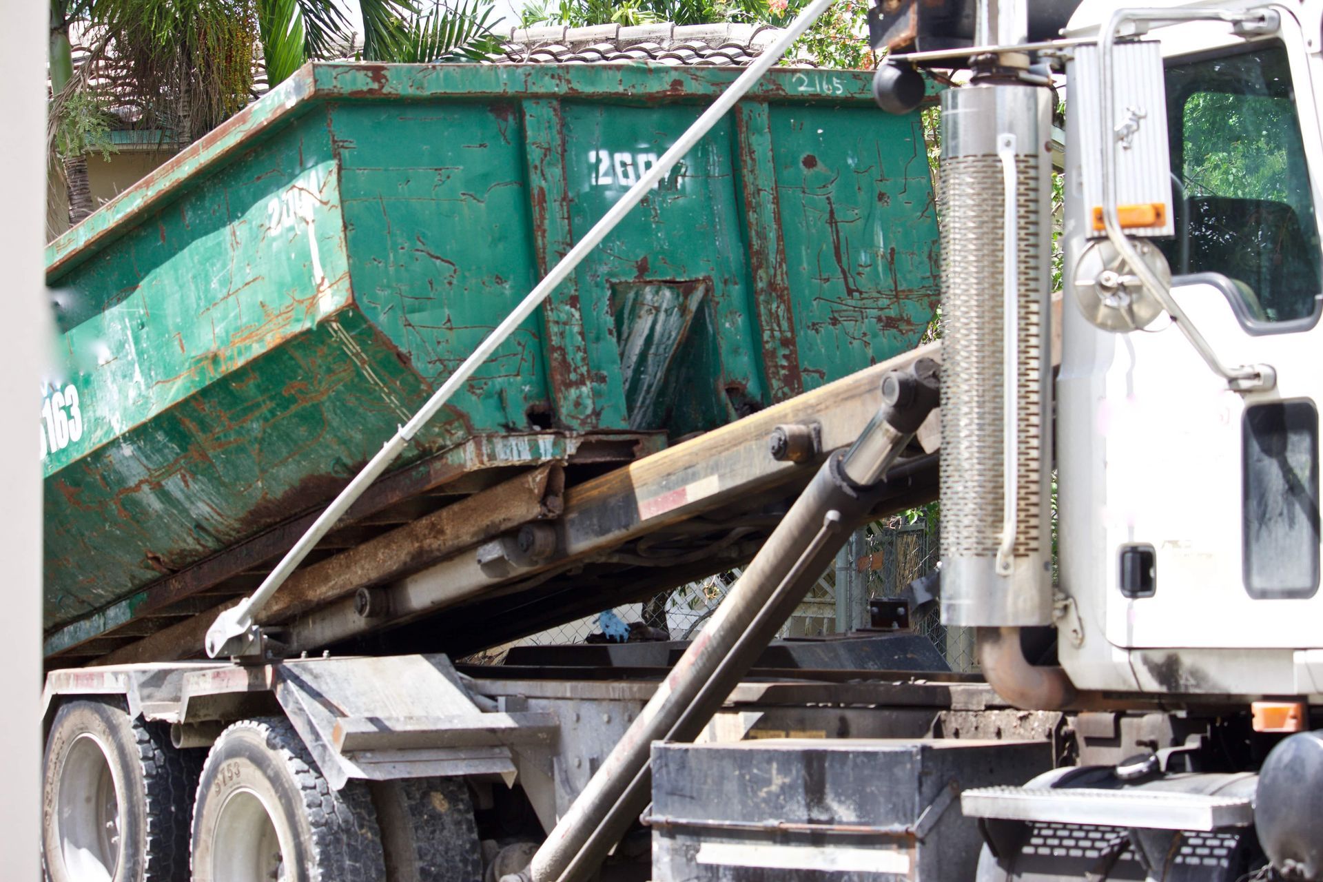 Green dump truck bed lifting on a white truck chassis at a construction site