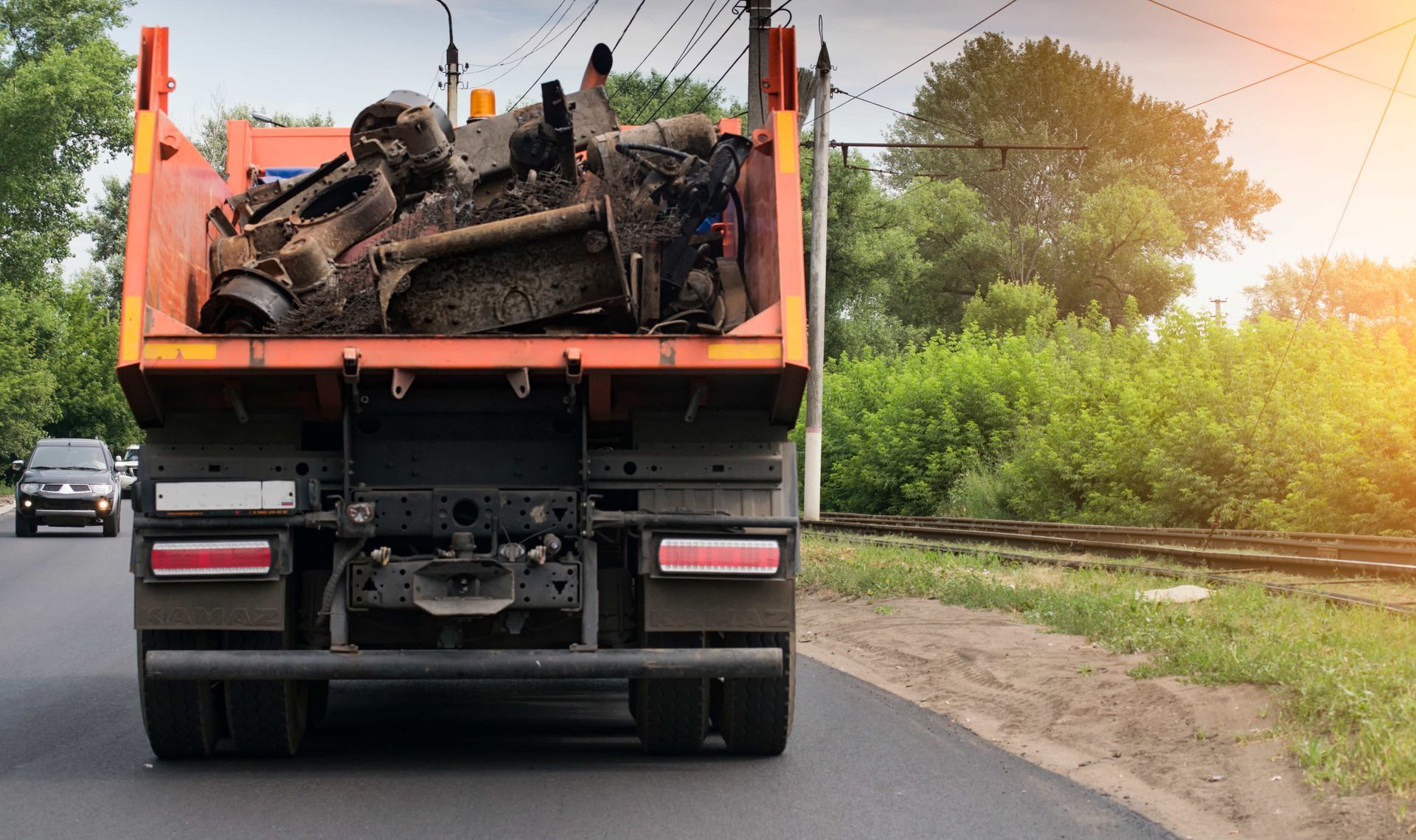 Dump truck carrying debris on a road beside greenery at sunset