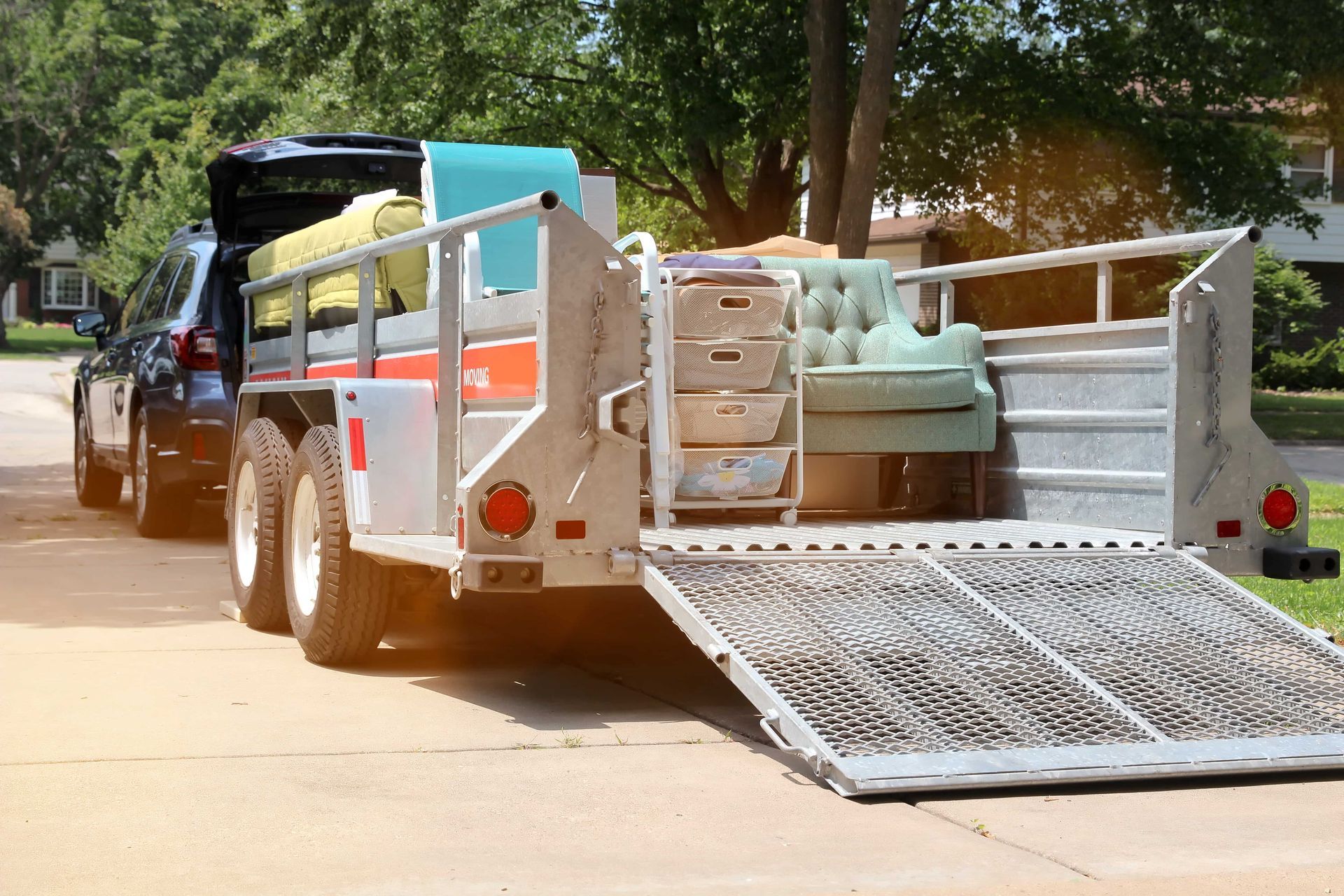 Truck trailer with a lowered metal ramp carrying furniture and boxes on a sunny residential street
