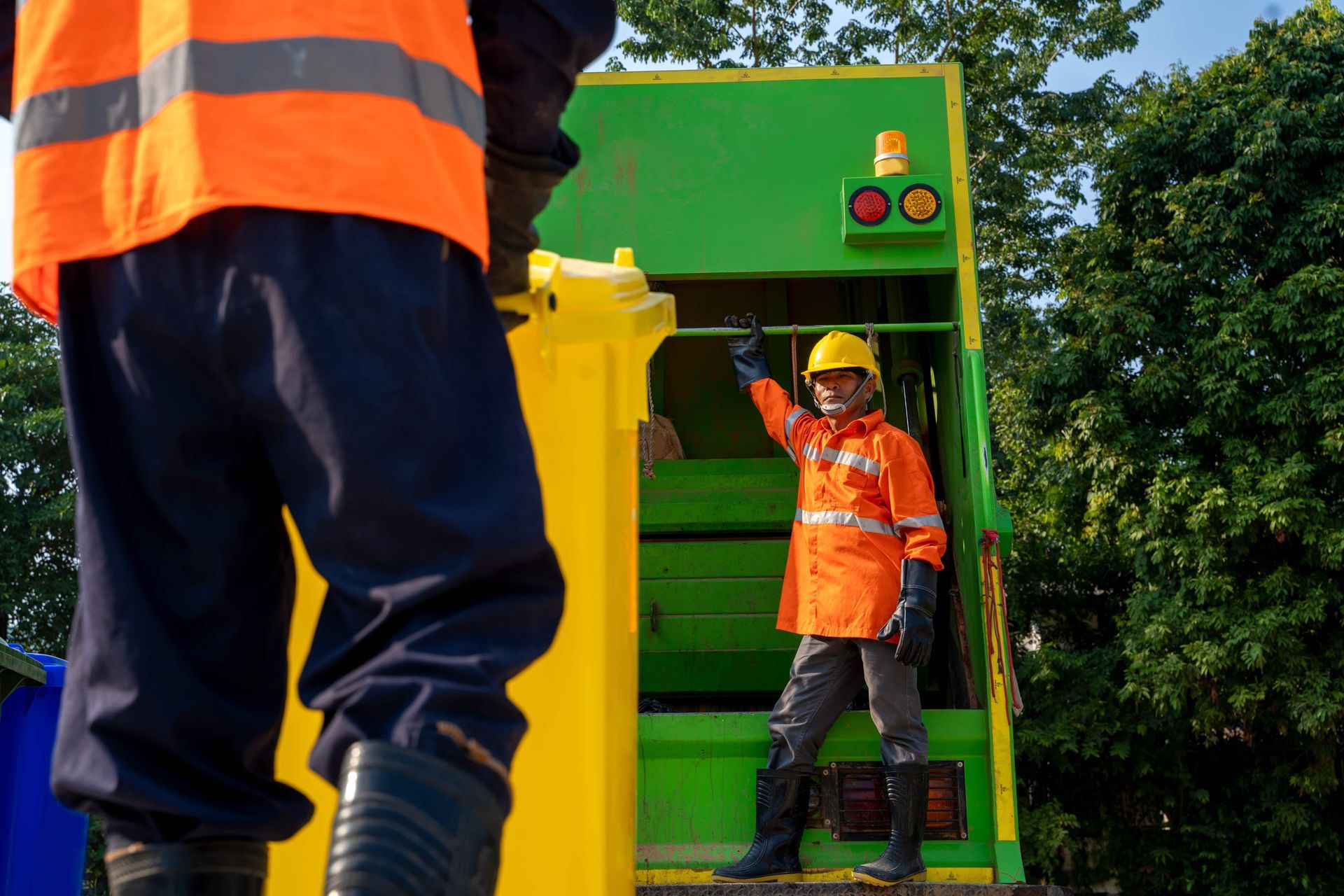 Two workers in orange safety gear stand by a green industrial machine outdoors.