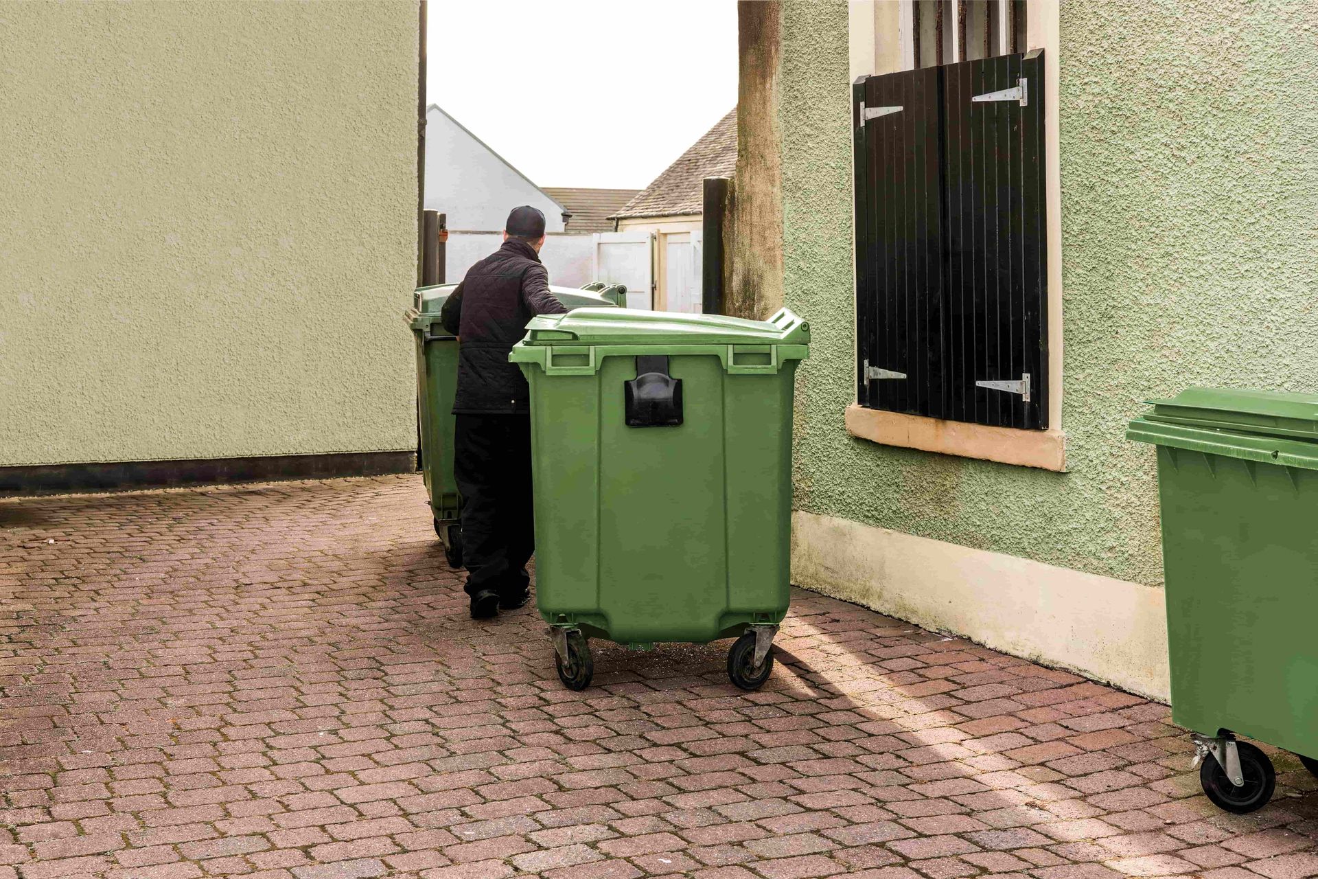 Worker beside green trash bin in a narrow alley between buildings
