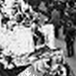 A black and white photo of a group of people standing around a table.