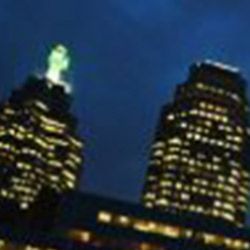 Two tall buildings are lit up at night with a blue sky in the background.