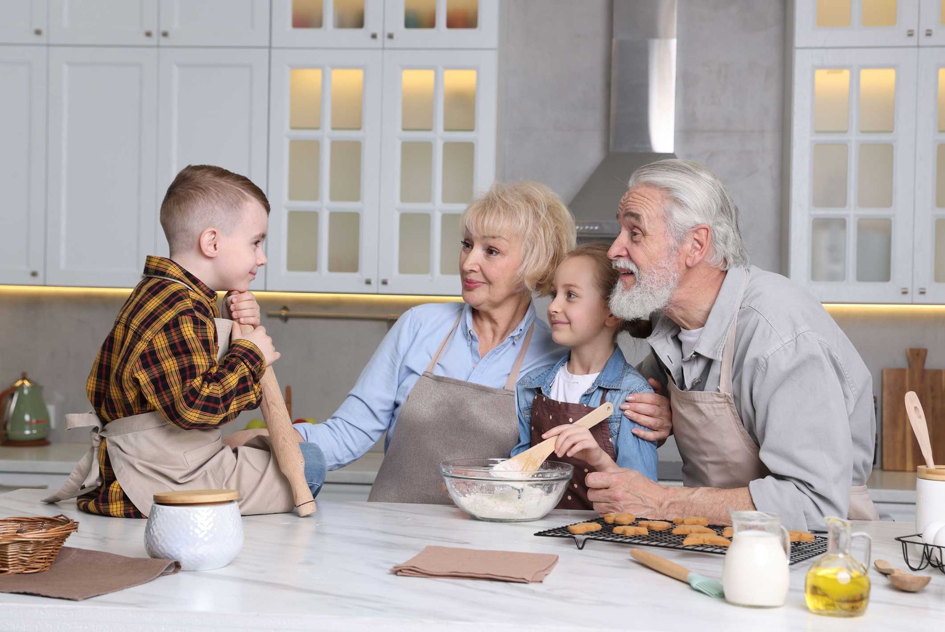 Family baking together in a bright kitchen: grandparents, boy, and girl smiling.