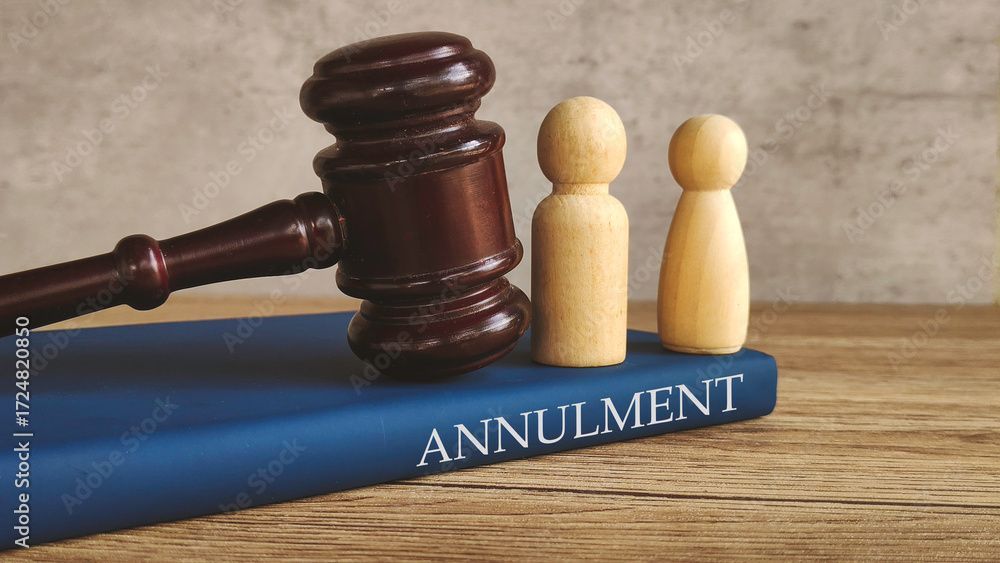 Two gold wedding bands rest on a wooden stand, with a gavel and paperwork blurred in the background. Two gold wedding bands rest on a wooden stand, with a gavel and paperwork blurred in the background.