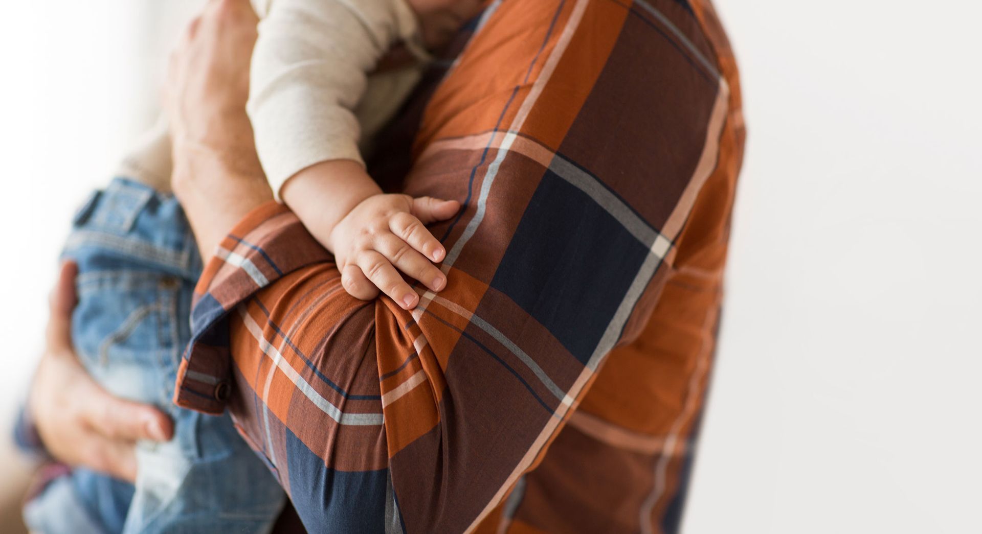 Person holding a baby; plaid shirt, baby's hand on caregiver's arm. Person holding a baby; plaid shirt, baby's hand on caregiver's arm.