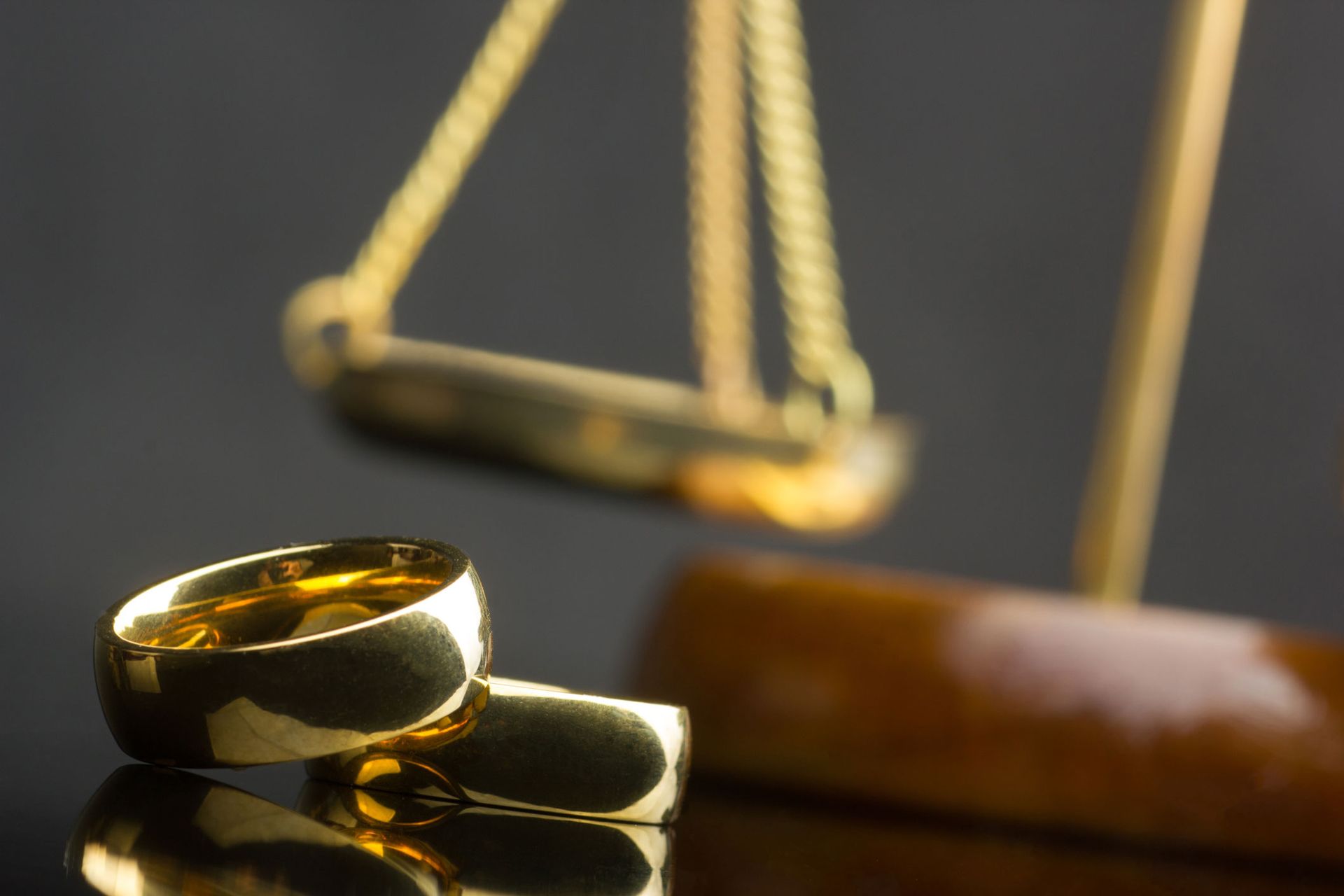 Gold wedding rings near a justice scale, symbolizing a divorce. Gold wedding rings near a justice scale, symbolizing a divorce.