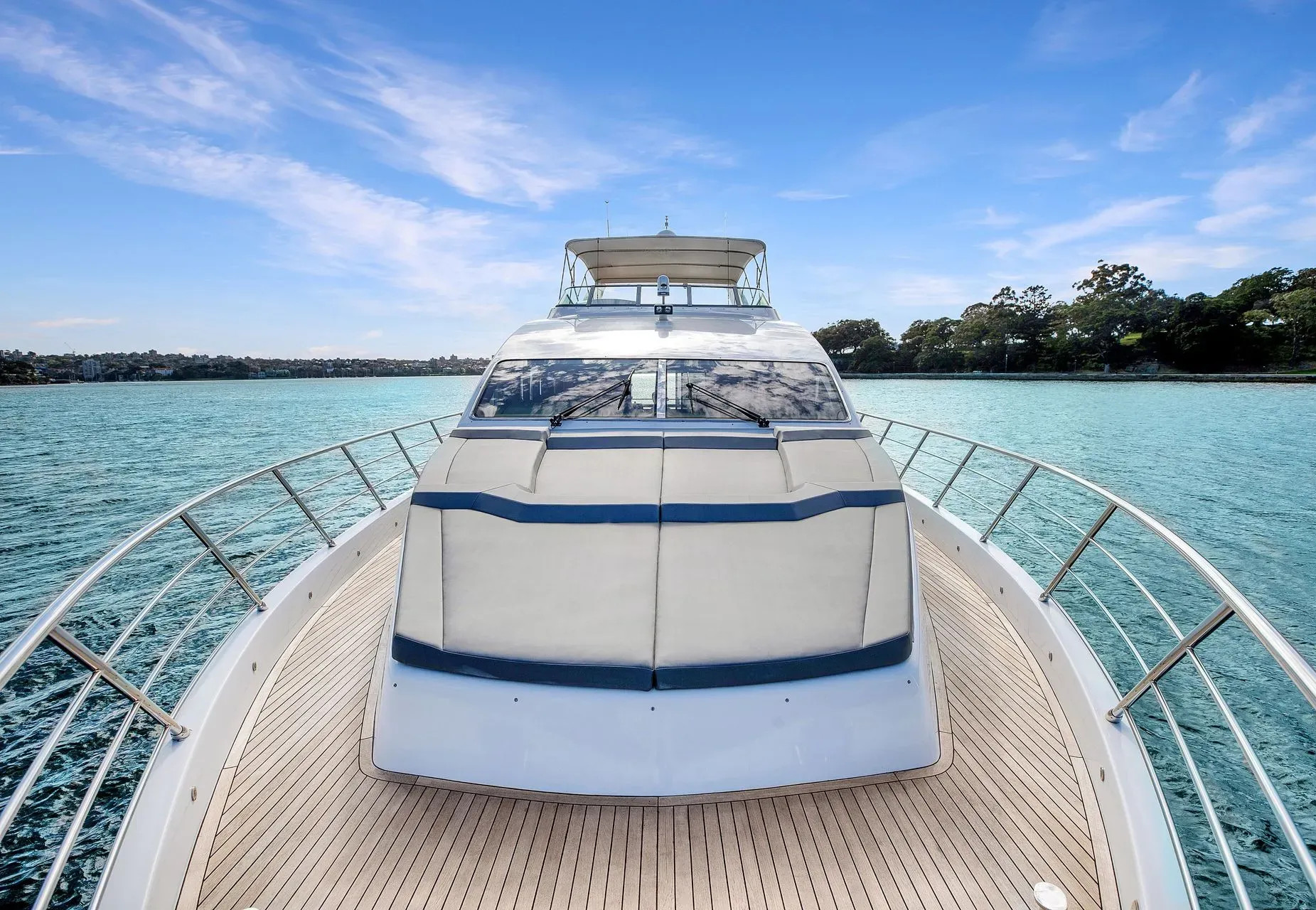 View from the bow of a yacht cruising on calm, bright blue tropical water under a clear sky.