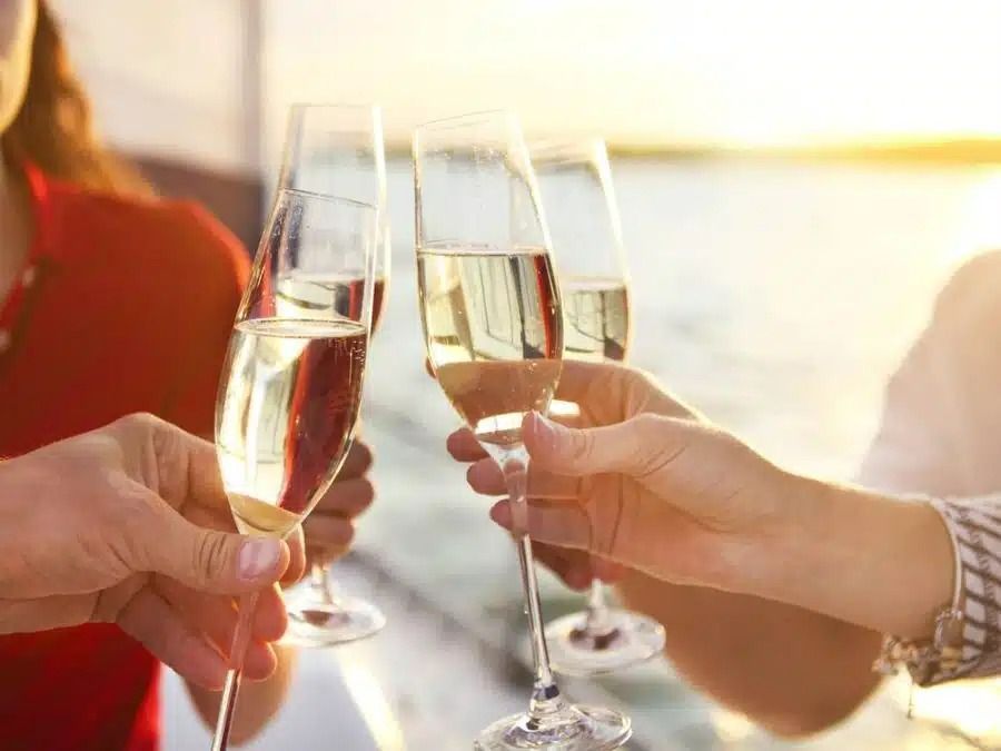 A group of friends laughing and relaxing on a sailboat on a sunny day, enjoying drinks and each other's company.