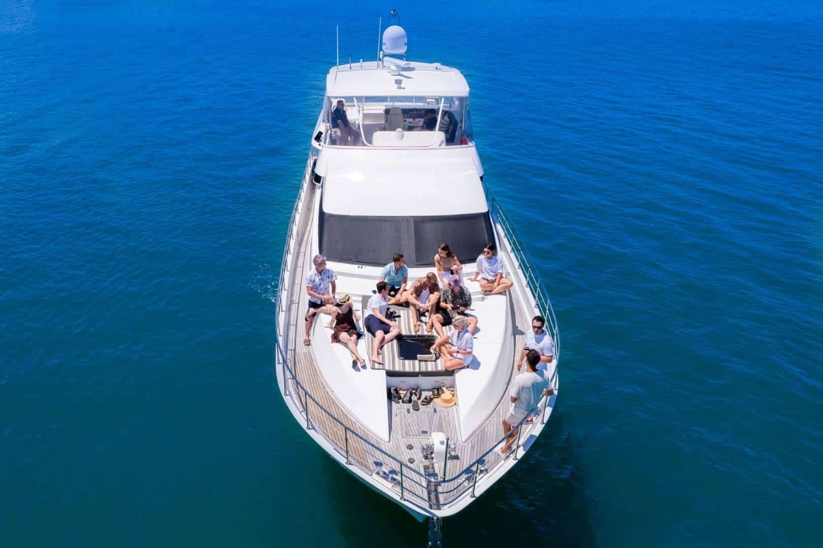 An aerial view of a white yacht on blue water with a group of people sitting on the deck enjoying the sun.