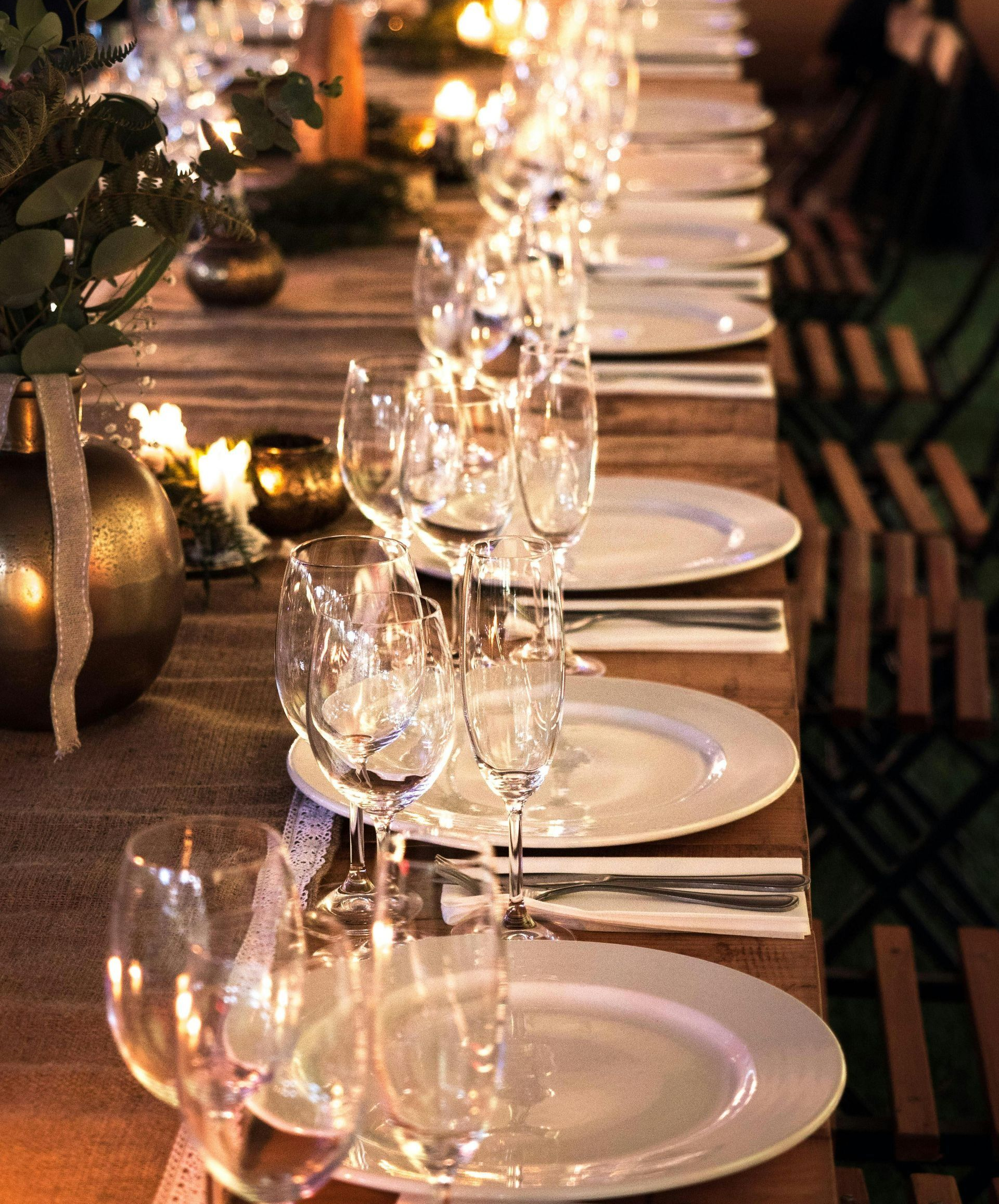 A long dinner table set with white plates, wine glasses, and candles, stretching into the background.