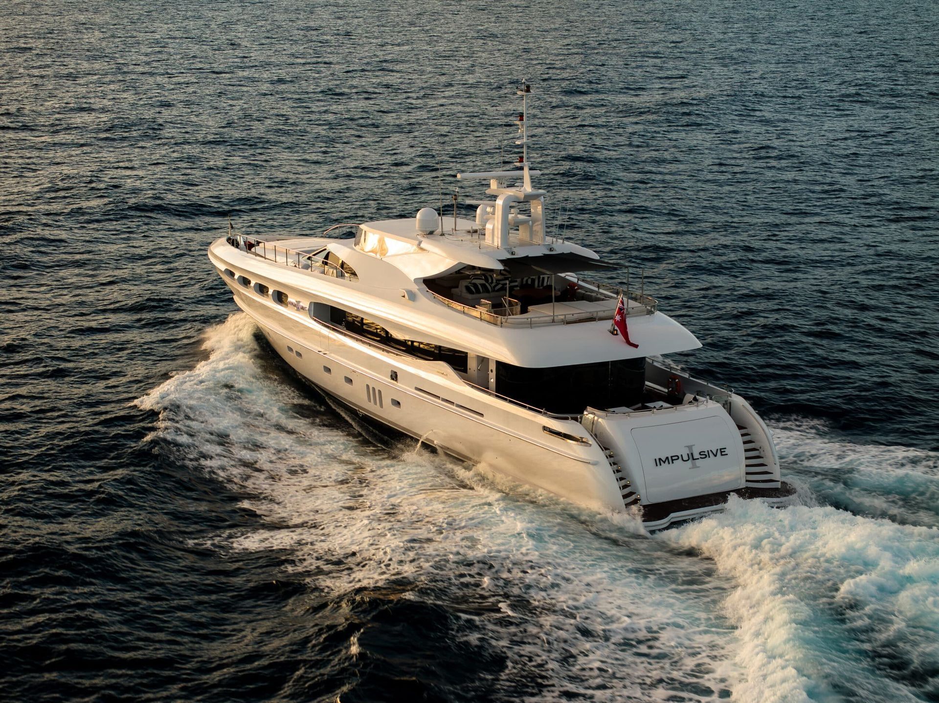 A white luxury yacht cruises across deep blue water, creating a wake as it moves forward.