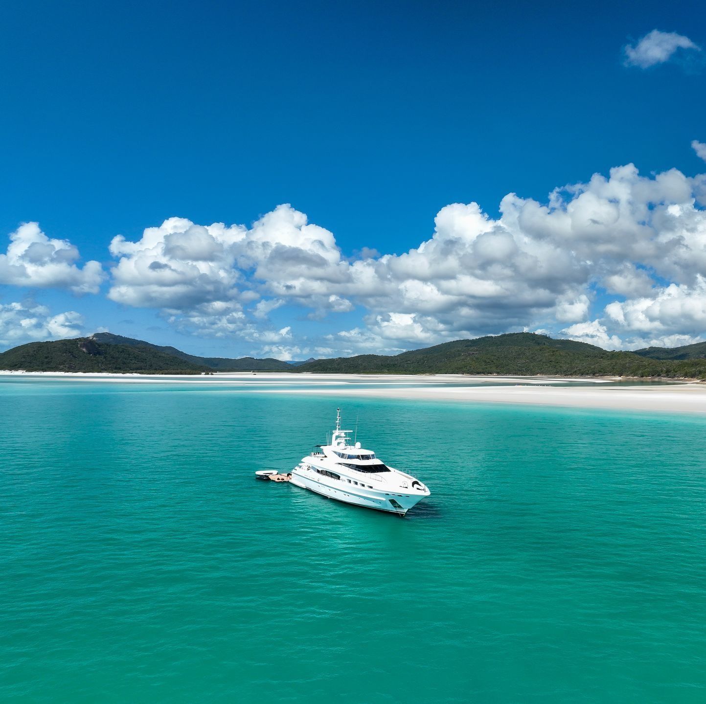People relaxing on a yacht and floating docks in clear turquoise water.