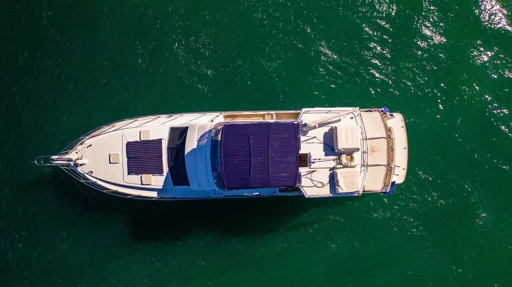 An overhead view of a white motor yacht with purple deck cushions floating on vibrant green ocean water.