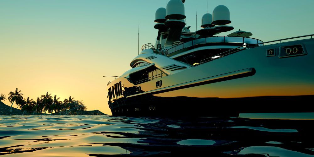 A white luxury yacht floats on calm, blue tropical water with a hilly, forested island in the background.