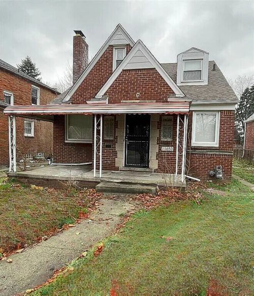 A brick house with a porch and a chimney on a cloudy day.