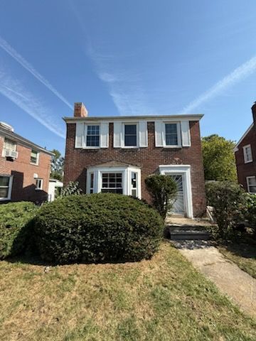 A large brick house with white shutters and a lush green yard.