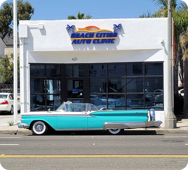 Turquoise classic car parked in front of Beach Cities Auto Clinic storefront