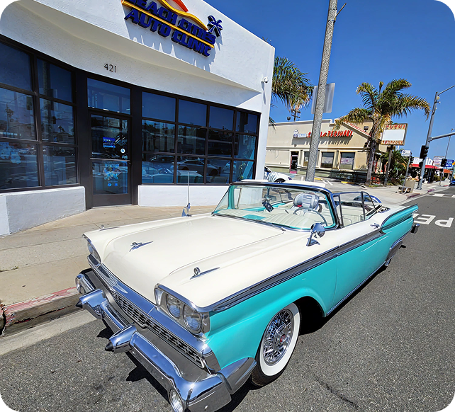 Classic turquoise-and-white convertible parked on a sunny street beside shops and palm trees