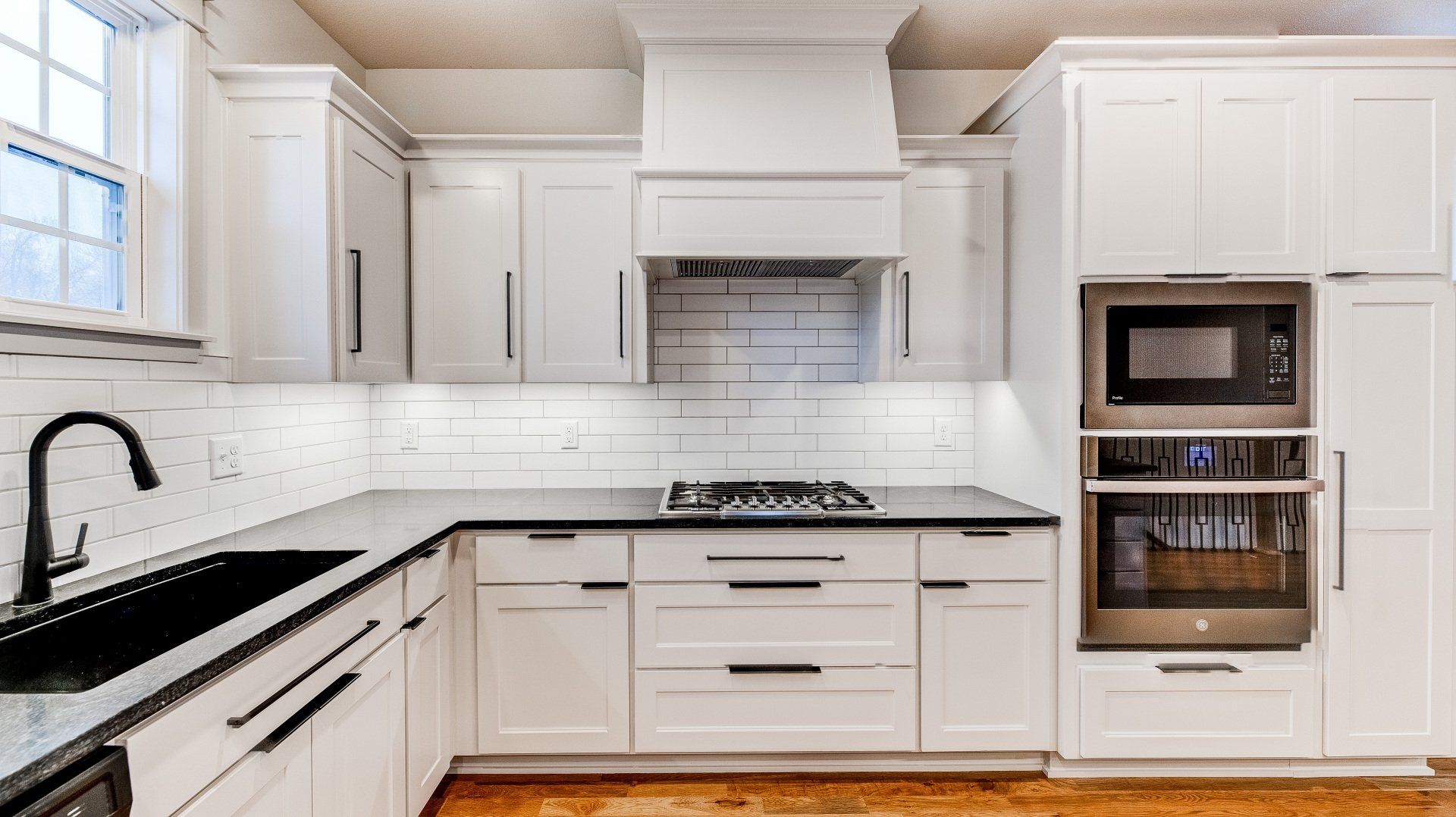A kitchen with white cabinets , black counter tops , stainless steel appliances and a sink.