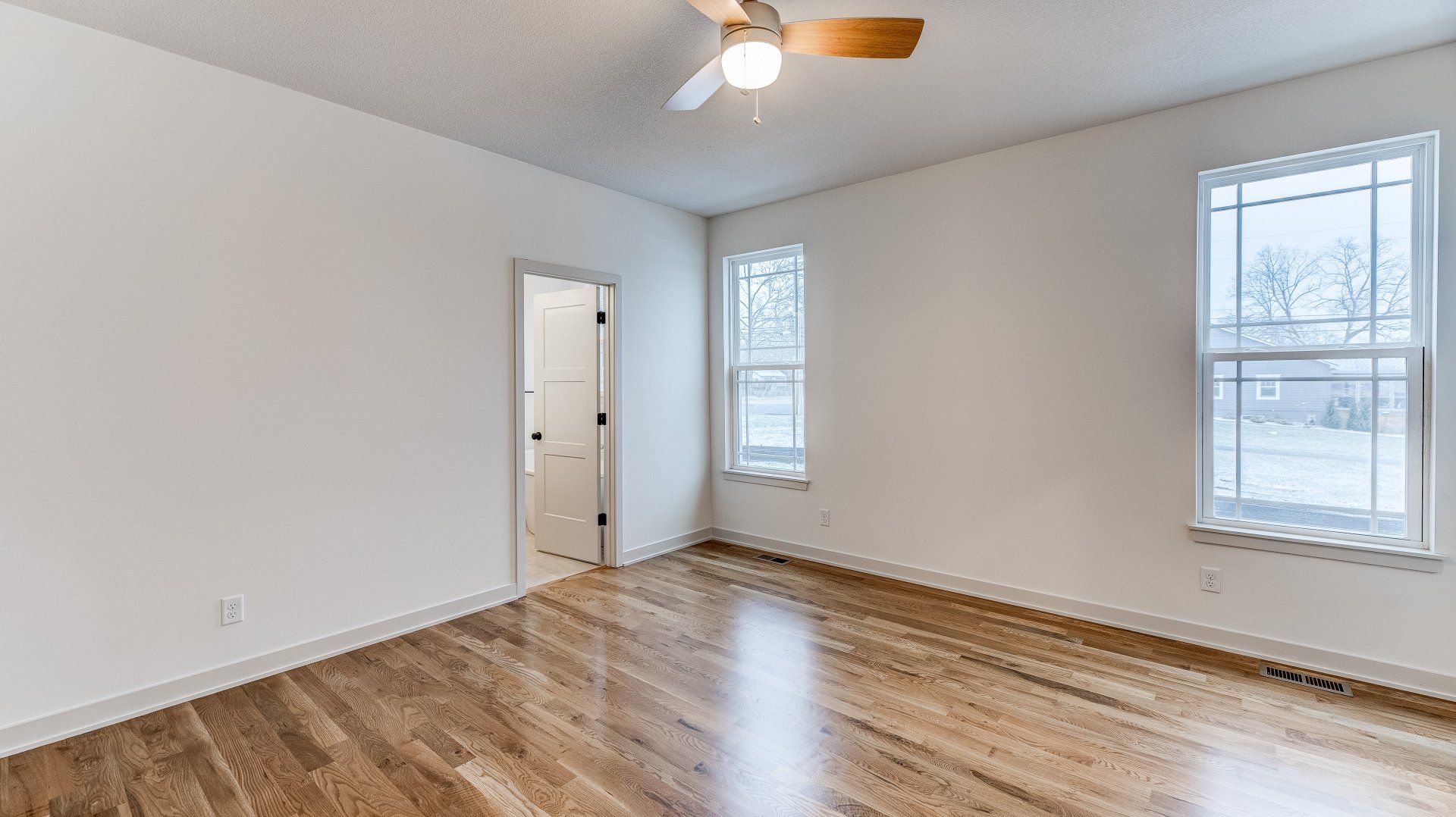 An empty room with hardwood floors and a ceiling fan.