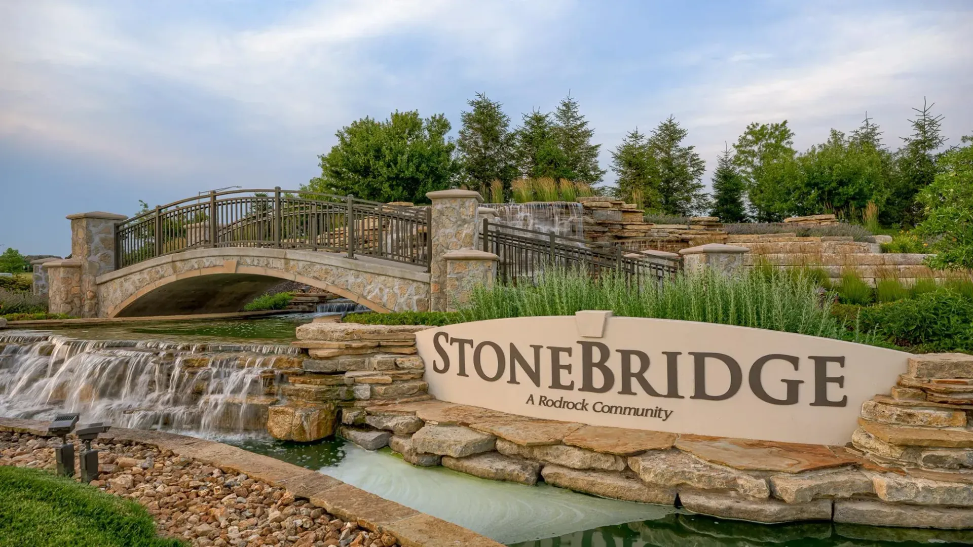 A stone bridge with a waterfall and a bridge in the background.