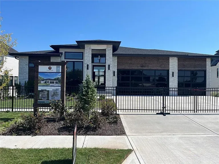Modern single-story building with large windows, black fence, and a paved driveway under a clear blue sky