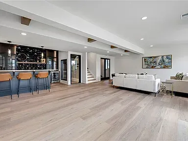 Modern open-plan living room with white sofas, wood floors, and a kitchen island with blue stools