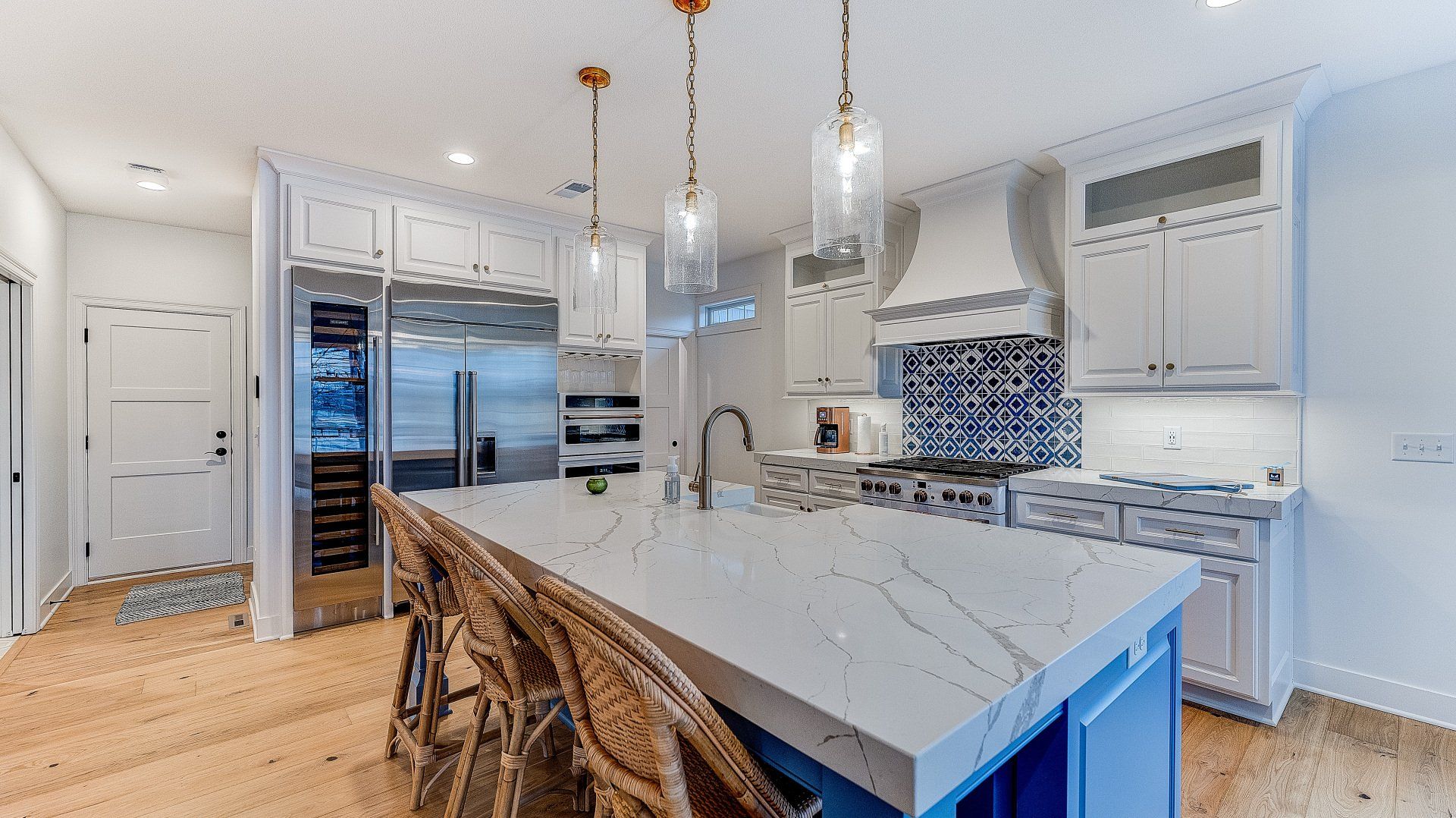 A kitchen with white cabinets , stainless steel appliances , a large island and wicker chairs.