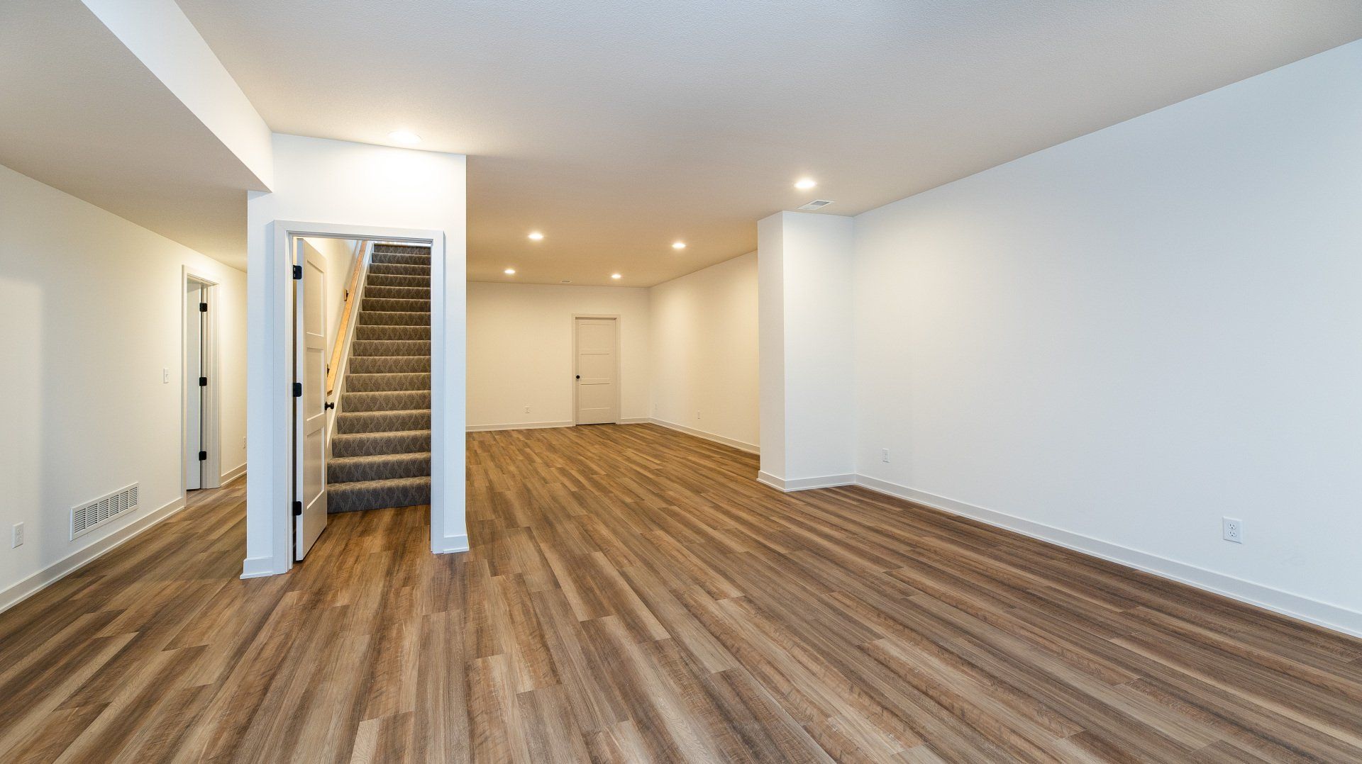 An empty basement with hardwood floors and white walls.