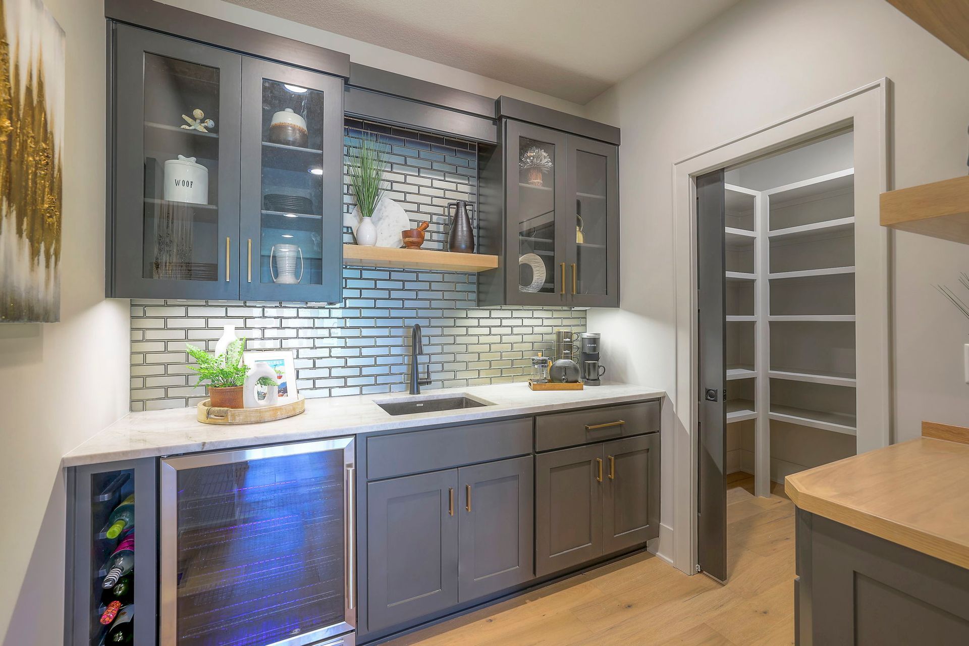 A kitchen with gray cabinets , a wine cooler , a sink , and a pantry.