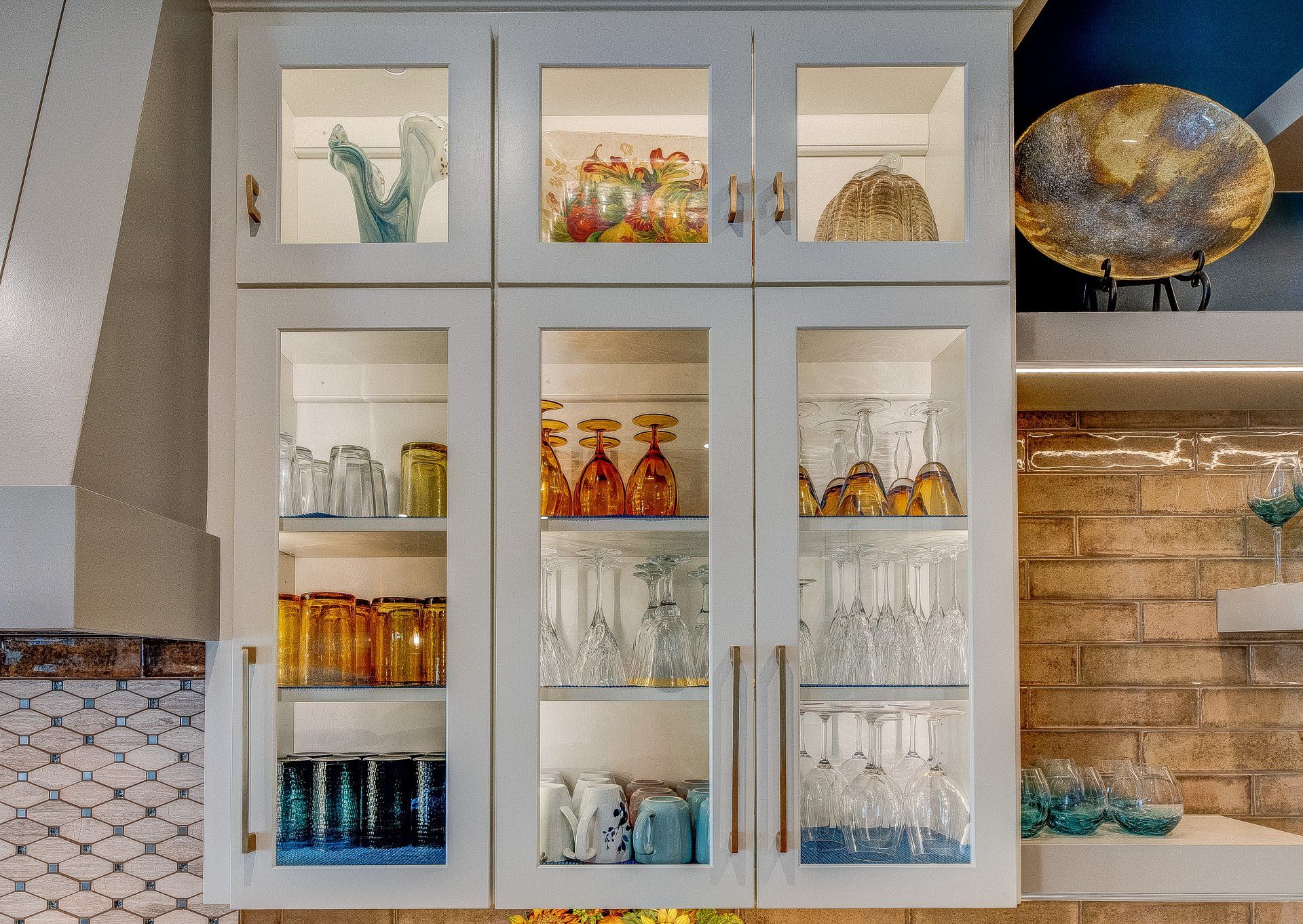 A kitchen with white cabinets and glass doors filled with glasses.