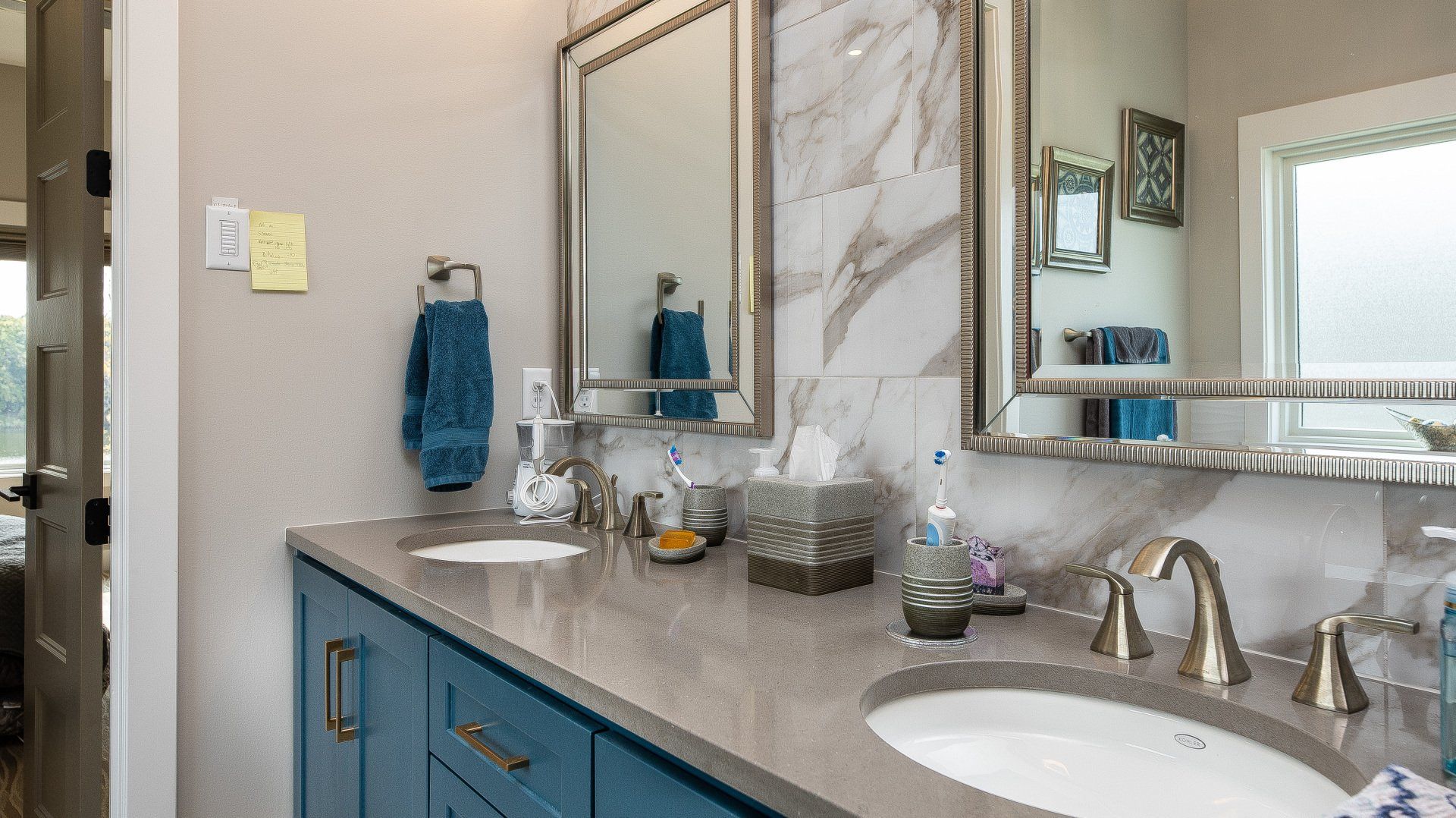 A bathroom with two sinks , two mirrors and blue cabinets.