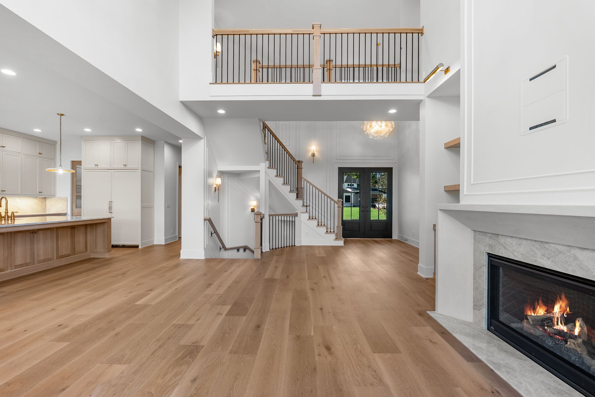 Spacious modern home interior with wooden floors, white walls, fireplace, and a staircase leading to a balcony.
